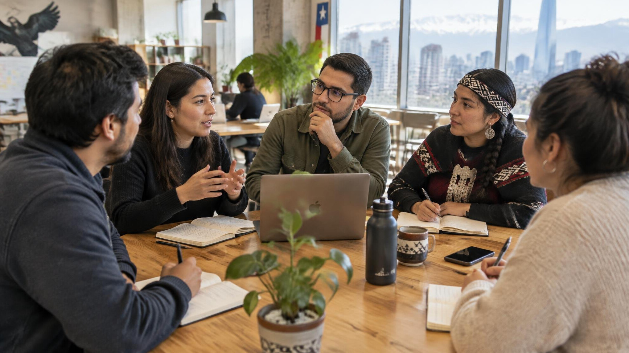 Group of young Chilean entrepreneurs discussing ideas around a table with notebooks and a laptop